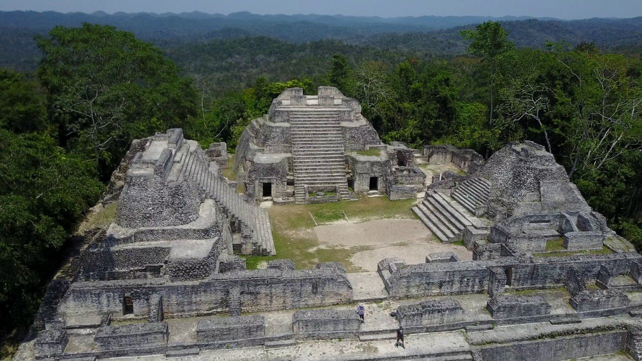 Aerial view of the Maya temple complex at Caracol, with stone staircases and plazas among forest and hills.