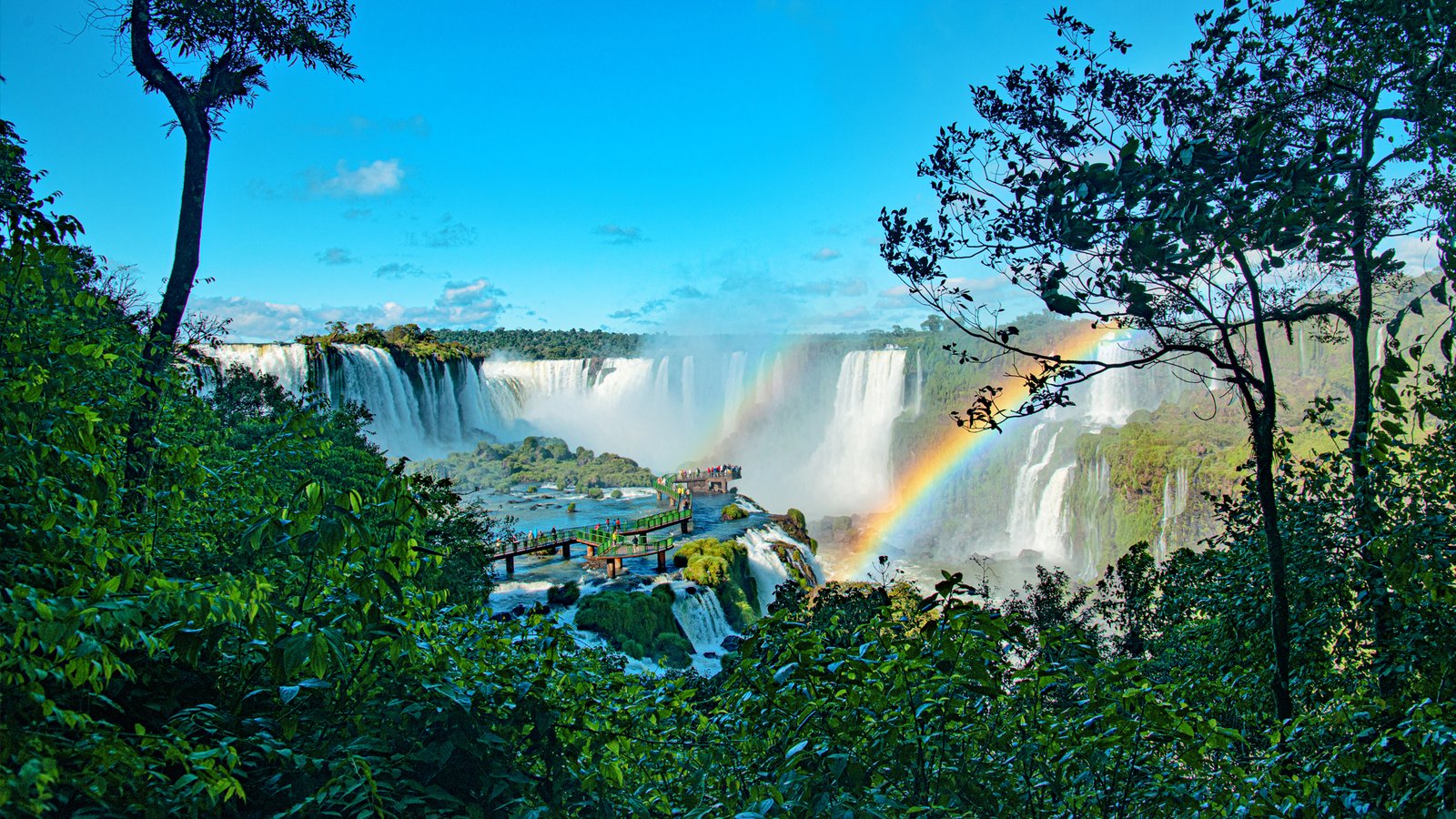 Iguazu Falls seen from a viewing platform with a rainbow arching over the cascades