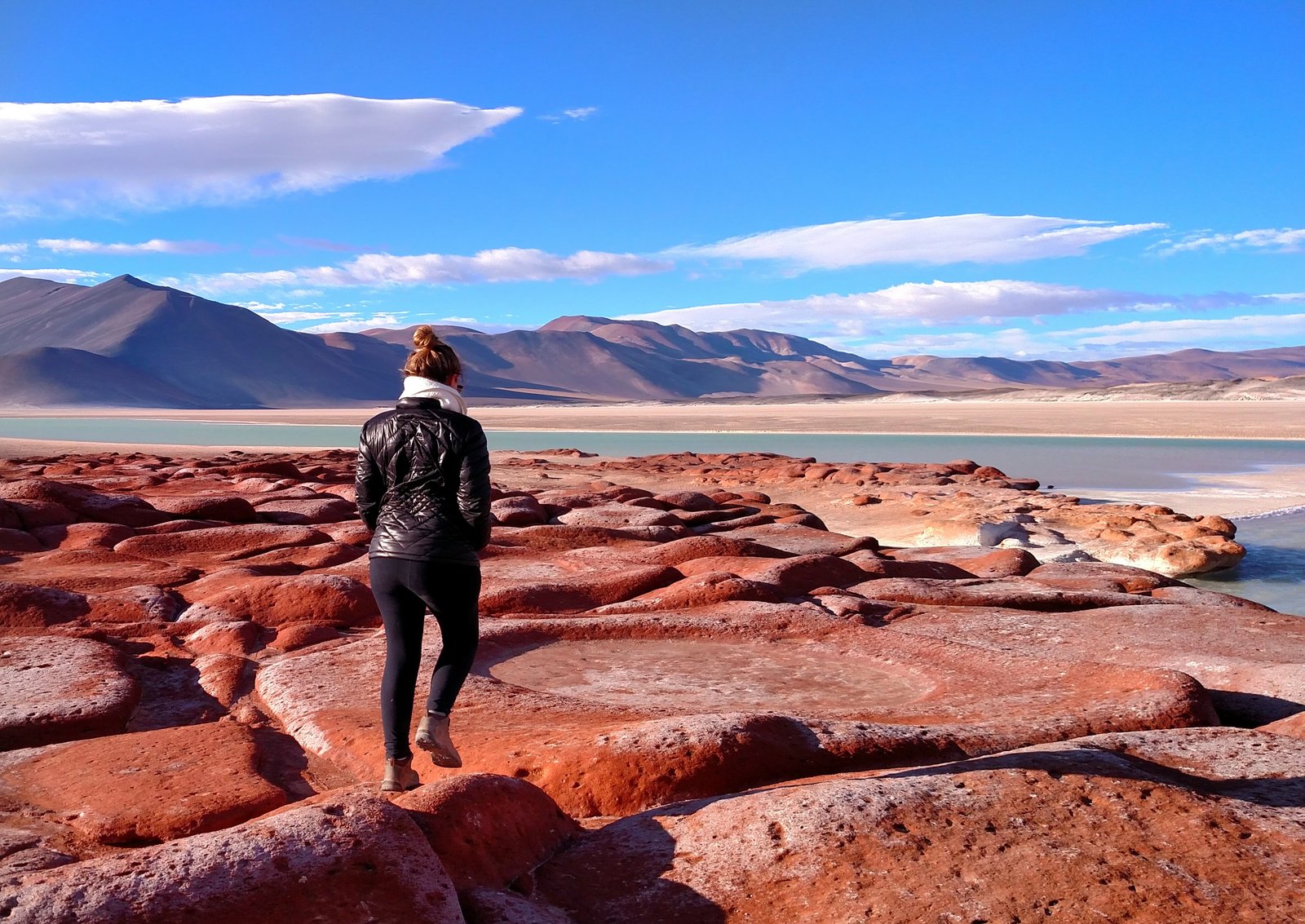 A traveller looks out over the red rock formations and salt flats of the Atacama Desert, Chile, at sunset.