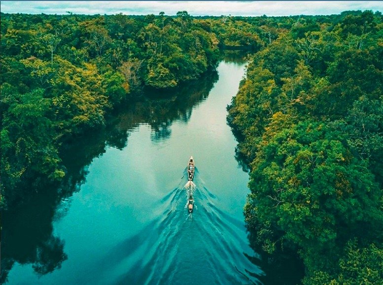 Aerial view of a boat navigating a river through the Amazon rainforest toward a forest lodge.