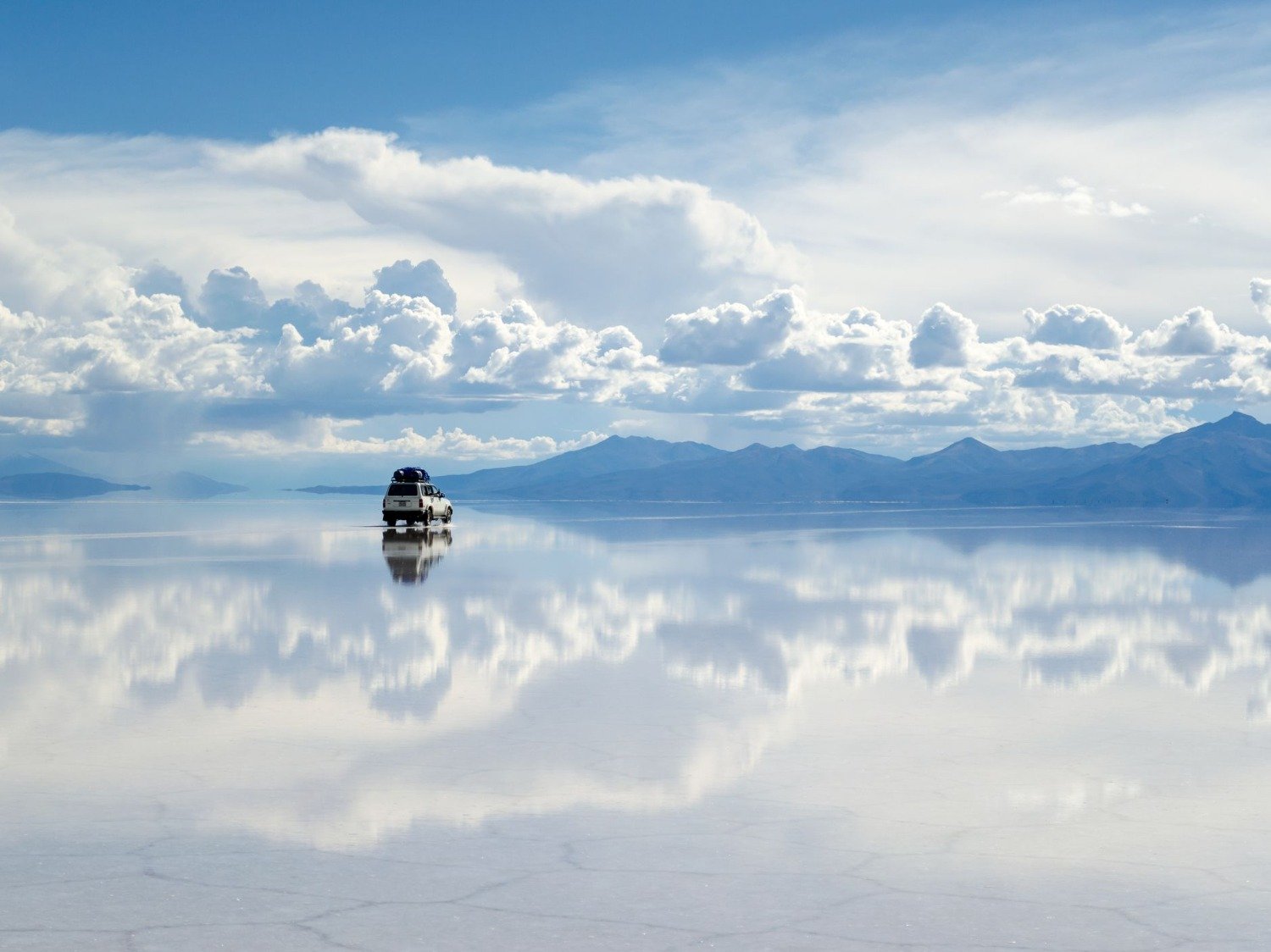 A four-wheel-drive vehicle reflected in shallow water on Bolivia's Uyuni salt flat.