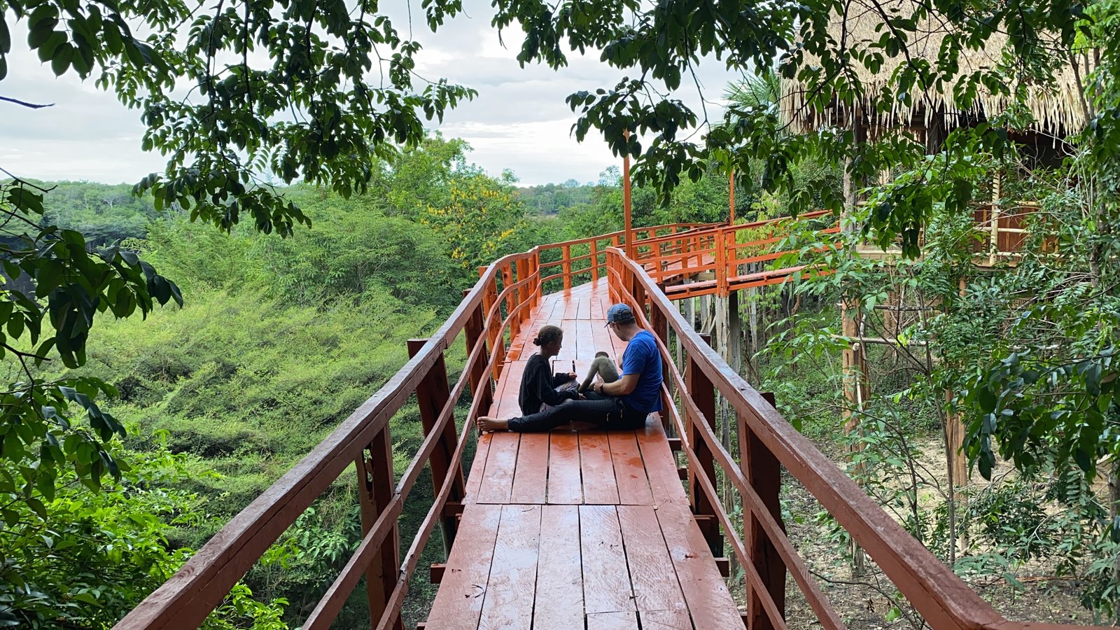 Two travellers sitting on a covered walkway at an Amazon lodge, overlooking the forest canopy.