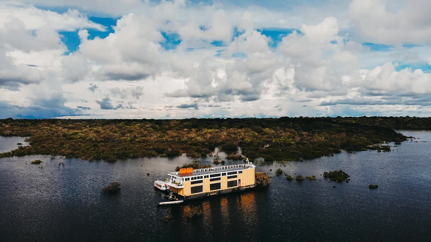 Small expedition vessel travelling through an Amazon waterway beneath a wide cloudscape