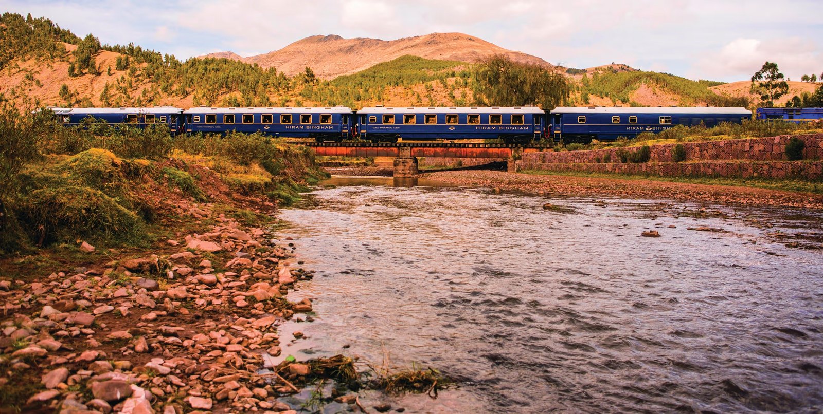 A blue luxury train crossing a bridge over a river on the route toward Machu Picchu, Peru.