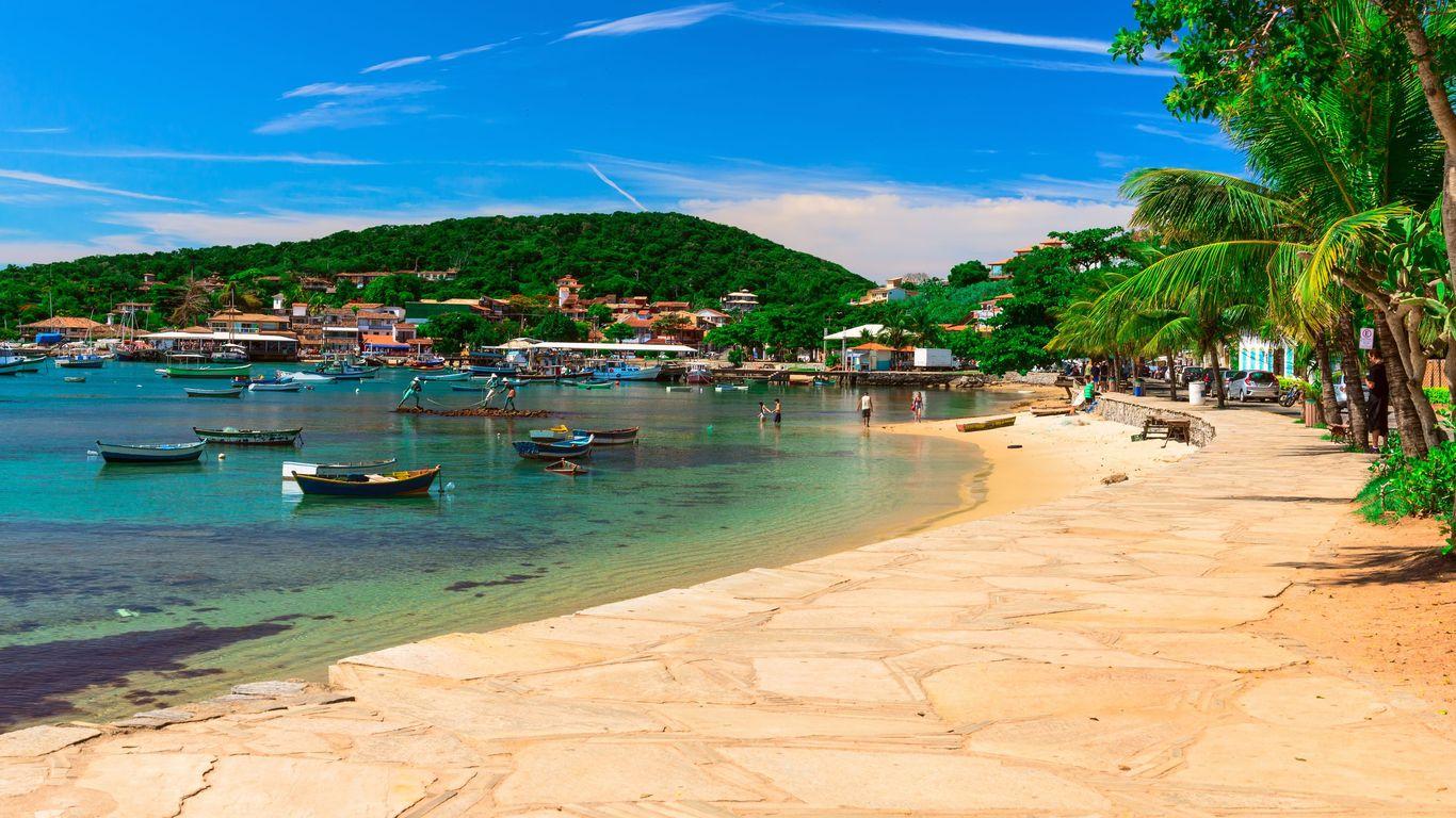 A family group walks along a sunlit beach promenade in Buzios, Brazil.