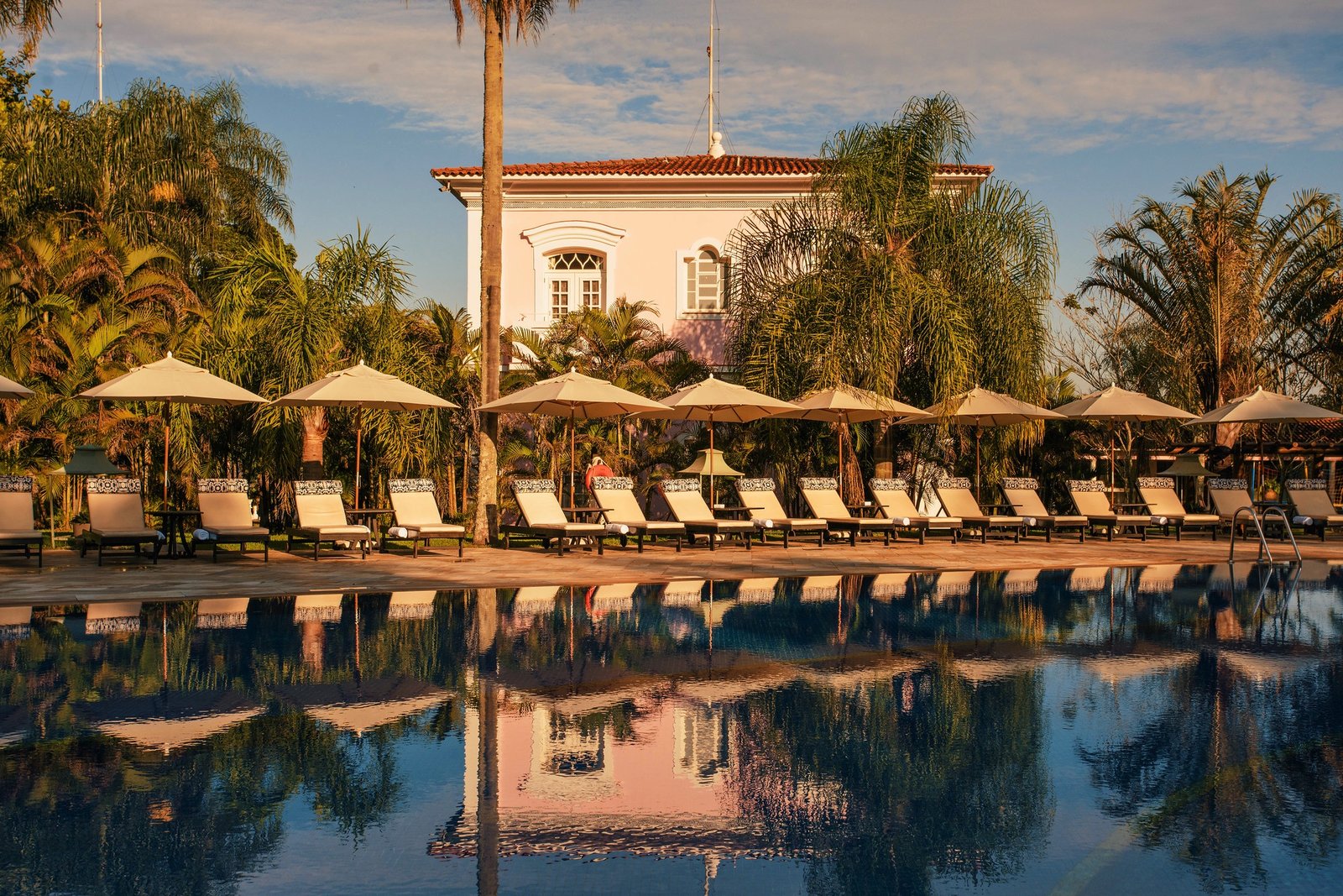 A quiet hotel pool lined with sun loungers and parasols in front of a colonial-style building near Iguaçu Falls.