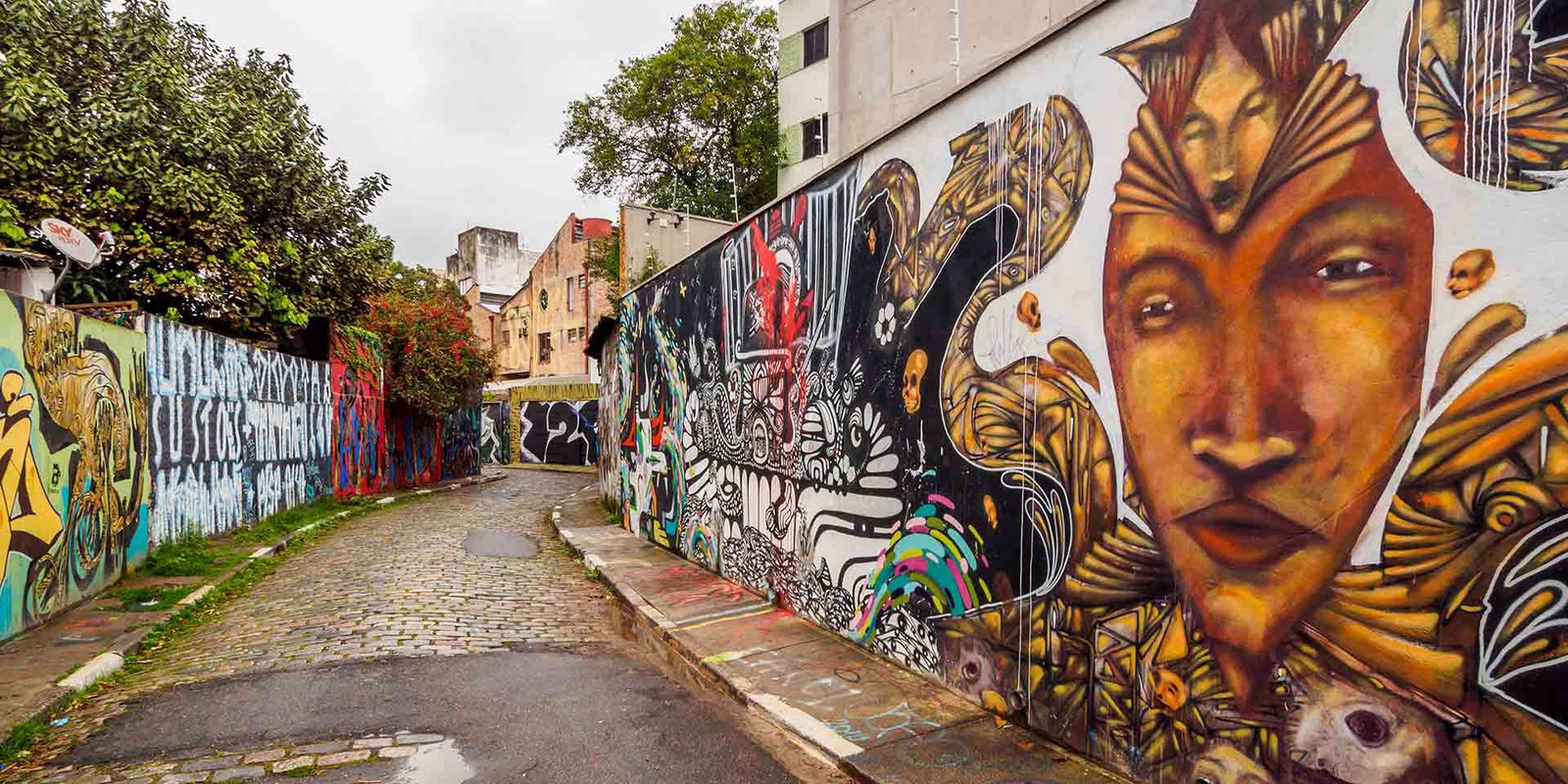 A street art-covered alley in São Paulo, with colourful murals lining both walls.