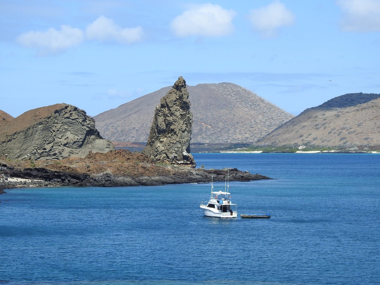 Pinnacle Rock on Bartolomé Island in the Galápagos, seen from the water with a small tour boat anchored offshore.