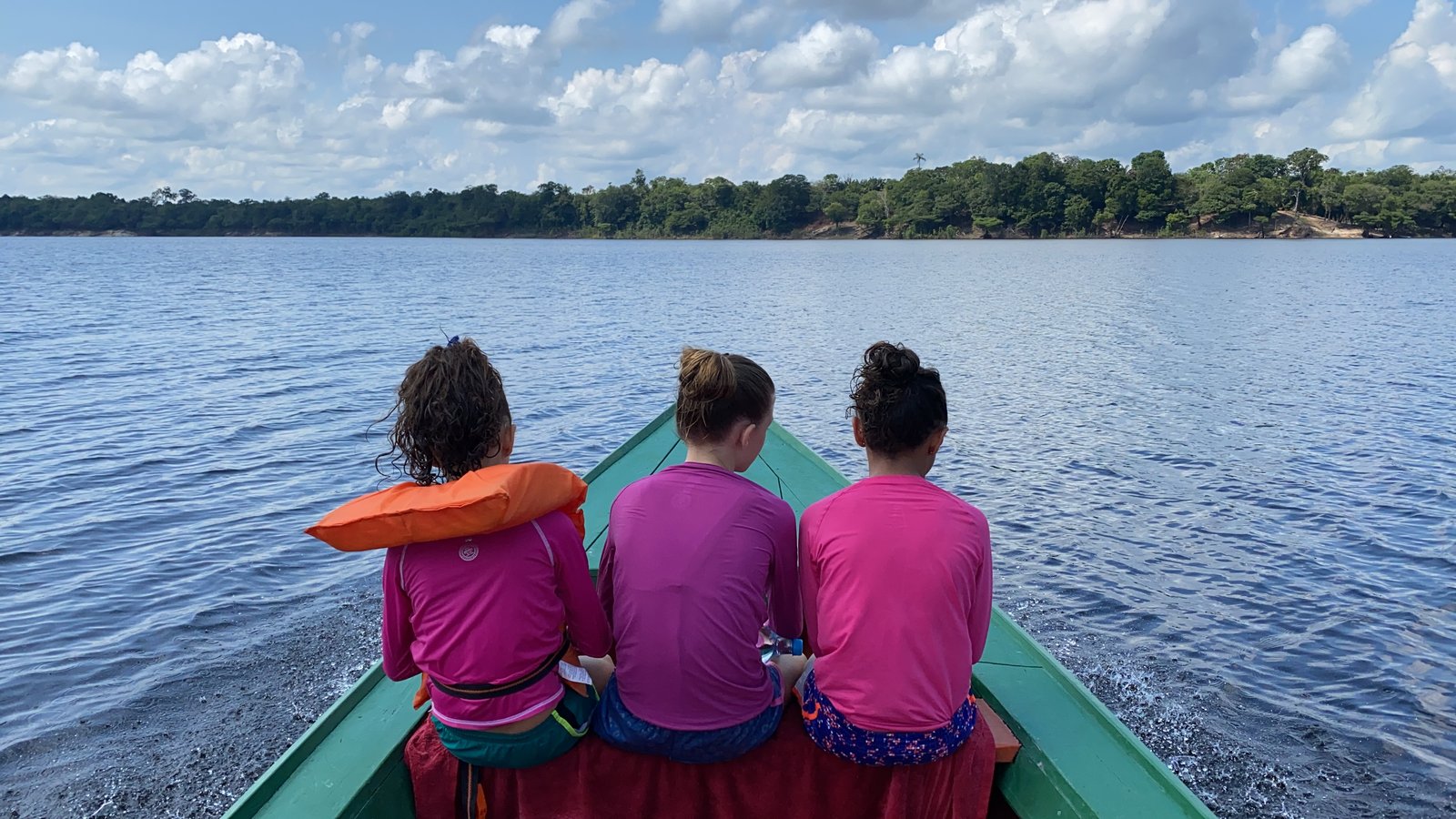 Travellers seen from behind in a small boat on a broad Amazon waterway.