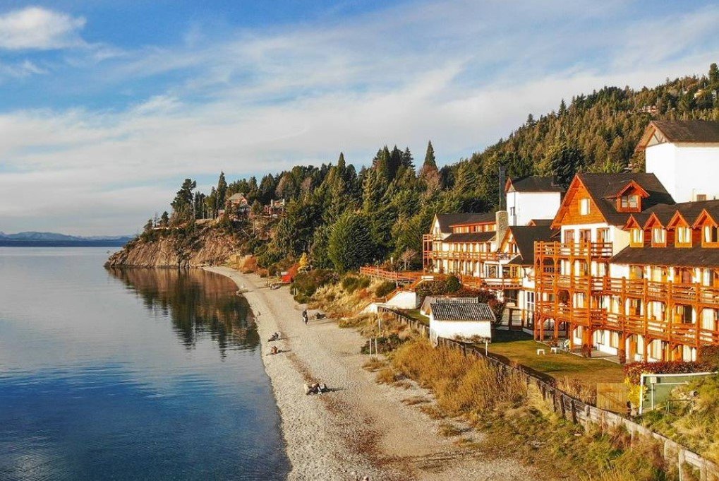 Wooden buildings beside a lake and wooded shore in Bariloche.