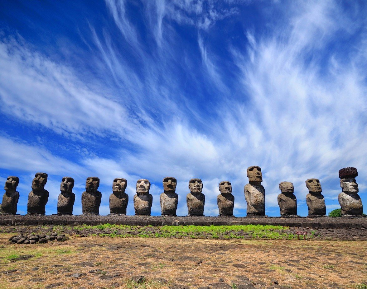 A row of moai statues on a stone platform on Easter Island under a blue sky.